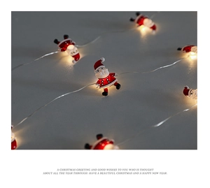 Close-up of LED Christmas light string featuring mini Santa Claus figurines on grey background