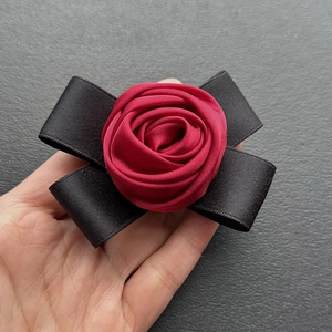 Detailed close-up of a burgundy fabric rose pin with a black satin bow accessory