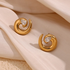 Macro shot of gold spiral stud earrings with water-drop zircon on champagne silk fabric