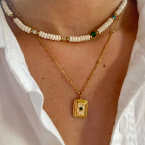 Detail of layered gold chain and white beaded necklace with emerald square pendant