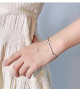 Detailed view of a silver cross bracelet on a model wrist with a minimalist design