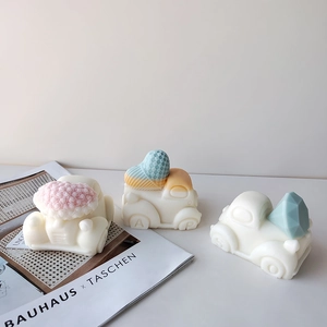 Three cute white car-shaped candles with floral and heart decorations on white surface