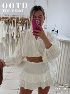 Close-up of white cotton two-piece set with V-neck button top and tiered ruffle skirt