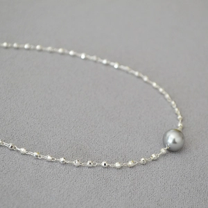 Close-up of a high-luster grey pearl on a delicate silver-tone beaded necklace chain