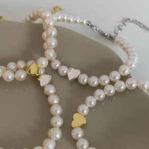 Close-up of freshwater pearl bracelet with gold and silver heart pendants in a ceramic tray
