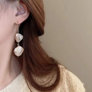 Primo piano di eleganti orecchini a goccia in conchiglia beige indossati da una modella