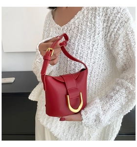 Detail of red leather shoulder bag featuring a large gold horseshoe buckle and matte finish