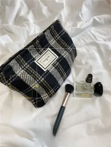 Close-up of plaid woven toiletry bag with Pleasant Time label on soft white bedding