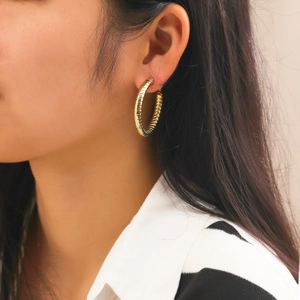 Detailed close-up of golden hollow hoop earring with stylish spiral ribbed texture