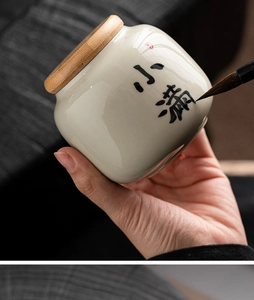 Close-up of a hand painting Chinese calligraphy on a ceramic tea canister with a brush