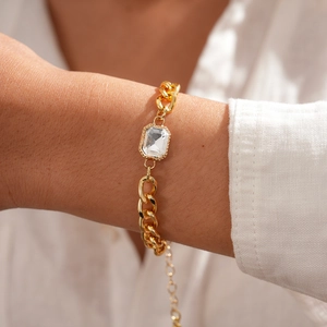Detailansicht eines goldfarbenen Kettenarmbands mit einem markanten rechteckigen Kristall