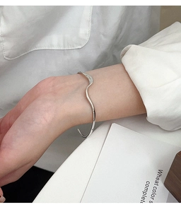 Dettaglio di un bracciale rigido ondulato in argento dallo stile minimalista al polso