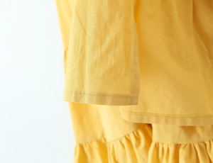 Detailed close-up of bright yellow dress featuring ruffled hem and cotton blend texture