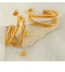 Macro shot of gold double U-shaped hoop earrings with butterfly and silicone backs on stone