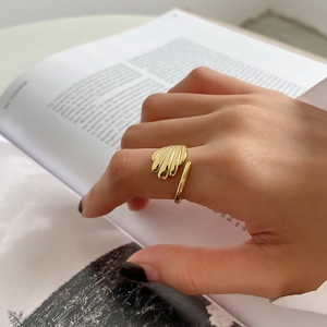 Detailed view of a gold shell-shaped sterling silver ring worn on a hand over a magazine