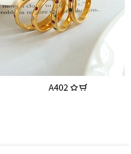 Detail of four gold minimalist rings with colorful inset stones on a white ceramic plate