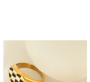 Détail d'une bague coeur dorée avec motif émaillé en damier noir et blanc sur le dessus