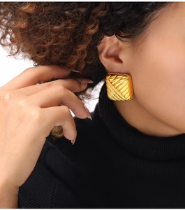 Gros plan de boucles d'oreilles carrées dorées à texture diagonale sur modèle
