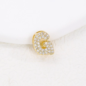 Detailed macro shot of golden letter G pendant with clear zircon stones on white surface