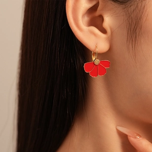 Detail of a red floral earring with gold metallic petal edges worn by a model
