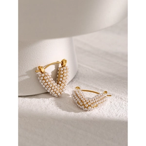 Minimalist V-shaped 18k gold earrings with white pearls on a textured white surface