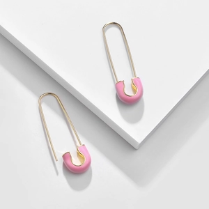 Detail view of pink enamel safety pin earrings on a white geometric display stand