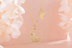 Détail du pendentif cheval à bascule doré sur chaîne sur fond floral rose