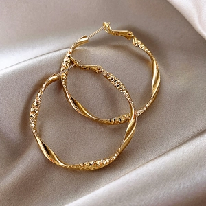 Golden twisted hoop earrings with diamond-cut texture on elegant champagne silk