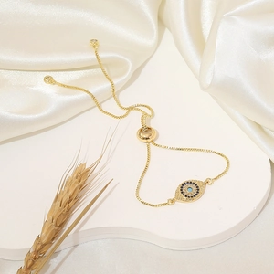 Macro shot of gold evil eye bracelet with blue zircon stones on white silk background