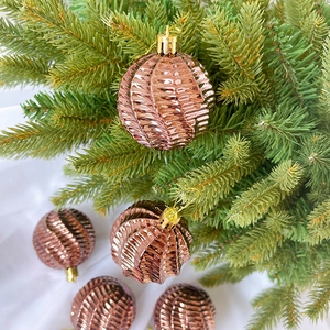 Detailaufnahme roségoldener Weihnachtskugeln mit Spiralstruktur an Tannenzweigen