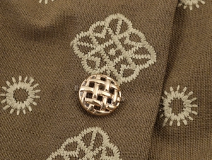 Macro de tissu marron avec broderie florale beige et un bouton doré en métal ajouré