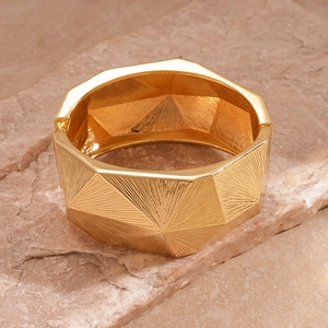 Close-up of golden geometric textured cuff bracelet on a natural stone background