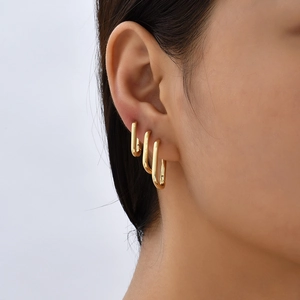 Close-up of three gold U-shaped minimalist hoop earrings stacked on a woman's ear