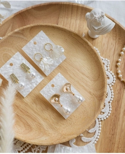 Flat lay of vintage gold and pearl earrings on wooden tray with lace and feathers