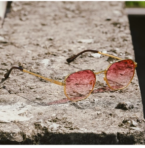 Close-up of retro gold metal sunglasses with pink gradient lenses on a stone surface