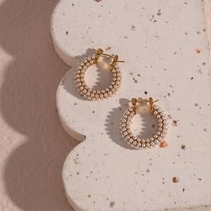 Close-up of gold plated hoop earrings with micro-set pearls on white textured stand