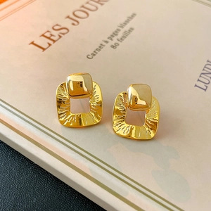 Detail of gold geometric square earrings with hammered texture on a vintage book