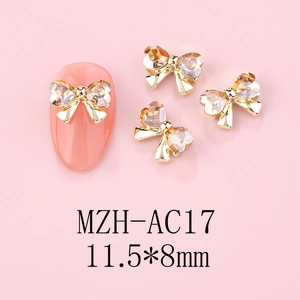 Macro view of 11.5x8mm gold heart bow nail charms with amber rhinestones on a pink tip