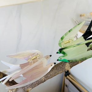 Swallow-shaped acetate hair claw clips in pink and green colors on a tree branch