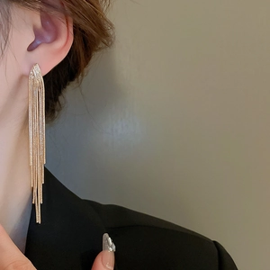 Detail of long gold V-shape chain tassel earrings worn with a black blazer
