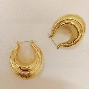 Détail macro de boucles d'oreilles créoles C dorées avec texture extérieure martelée unique
