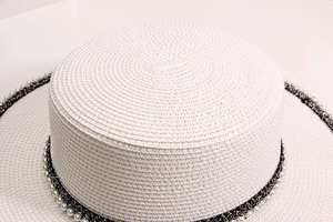 Detail showing woven white straw texture and pearl trim on the boater hat crown
