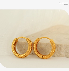 Detailed close-up of golden hoop earrings with textured spiral design on stone surface
