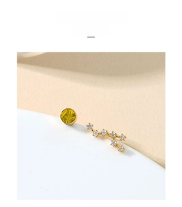 Detailed view of asymmetric gold stud earrings featuring a yellow stone and star constellation