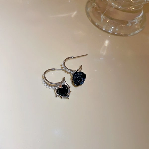 Detail of asymmetric silver needle earrings featuring black heart, rose, and small pearls