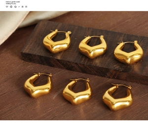 Detail of bold gold geometric V-shaped earrings on rustic wood with silk accents