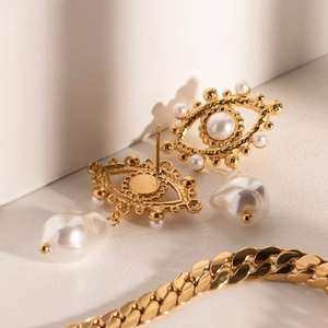 Detailed close-up of gold evil eye earrings with white pearls and textured metal