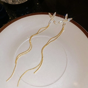 Détail des boucles d'oreilles à pompon doré avec papillon en zircon sur assiette blanche