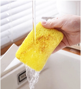 Close-up of a hand rinsing a yellow cellulose sponge under flowing water in kitchen
