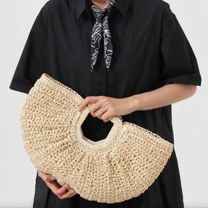 Handwoven straw tote bag with half-moon design held by model in black dress